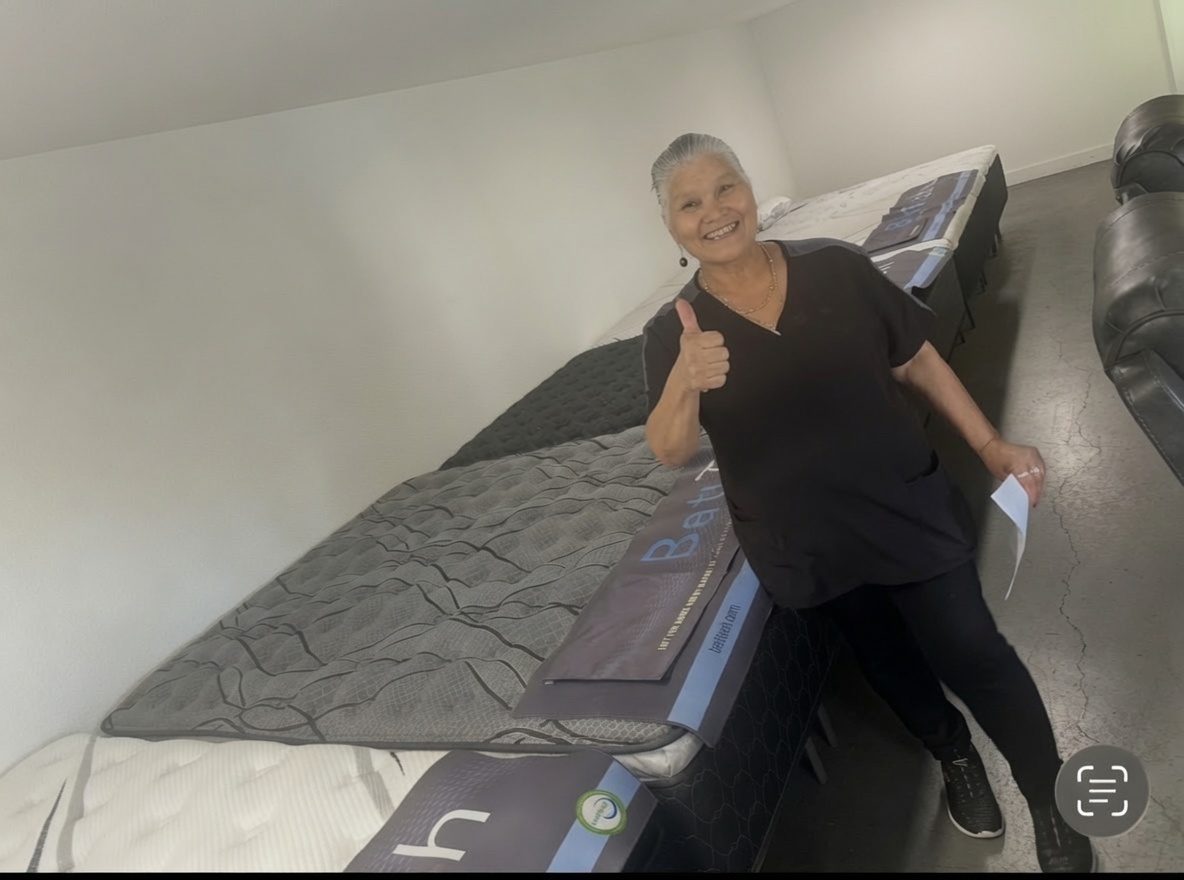 Rows of brand new mattresses at the mattress warehouse in Elk Grove with a happy customer giving a thumbs up